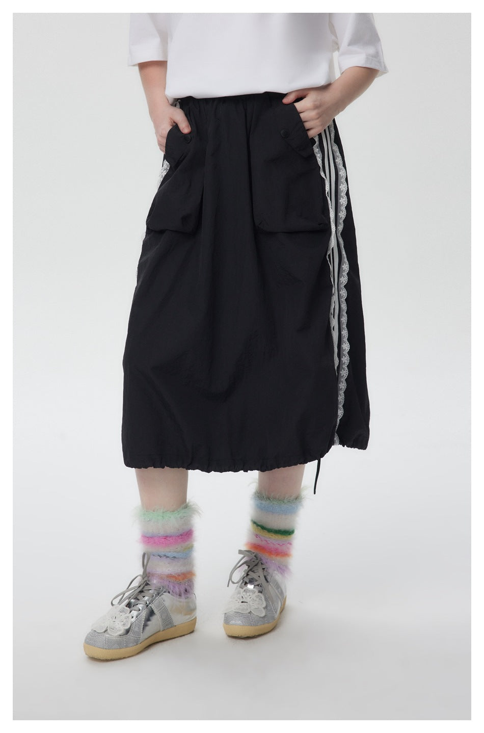 Cropped model wearing the front of a black midi skirt with large buttoned pockets and white lace-edged side stripes.