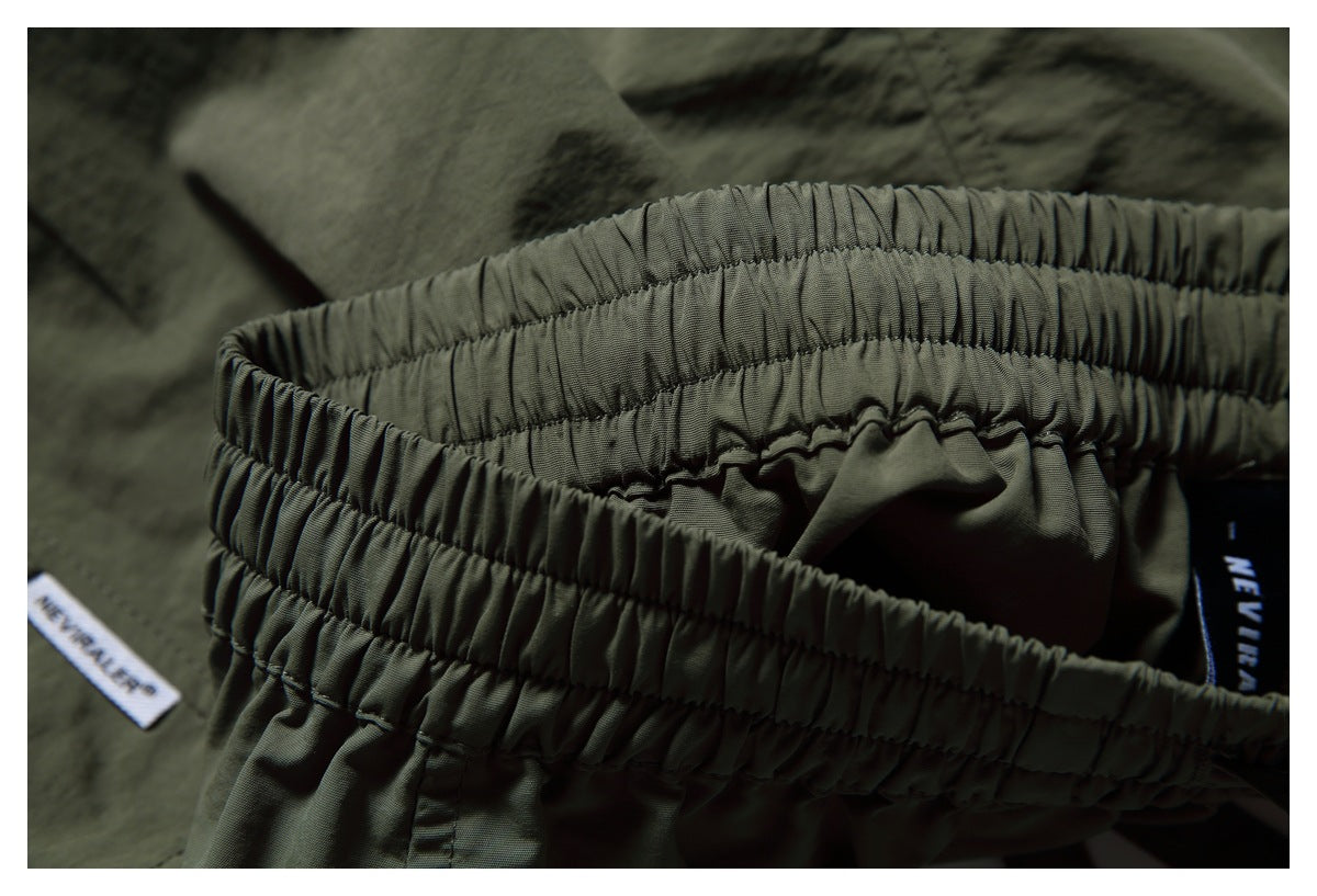 Close-up of the gathered elastic waistband and inner label of dark olive shorts.