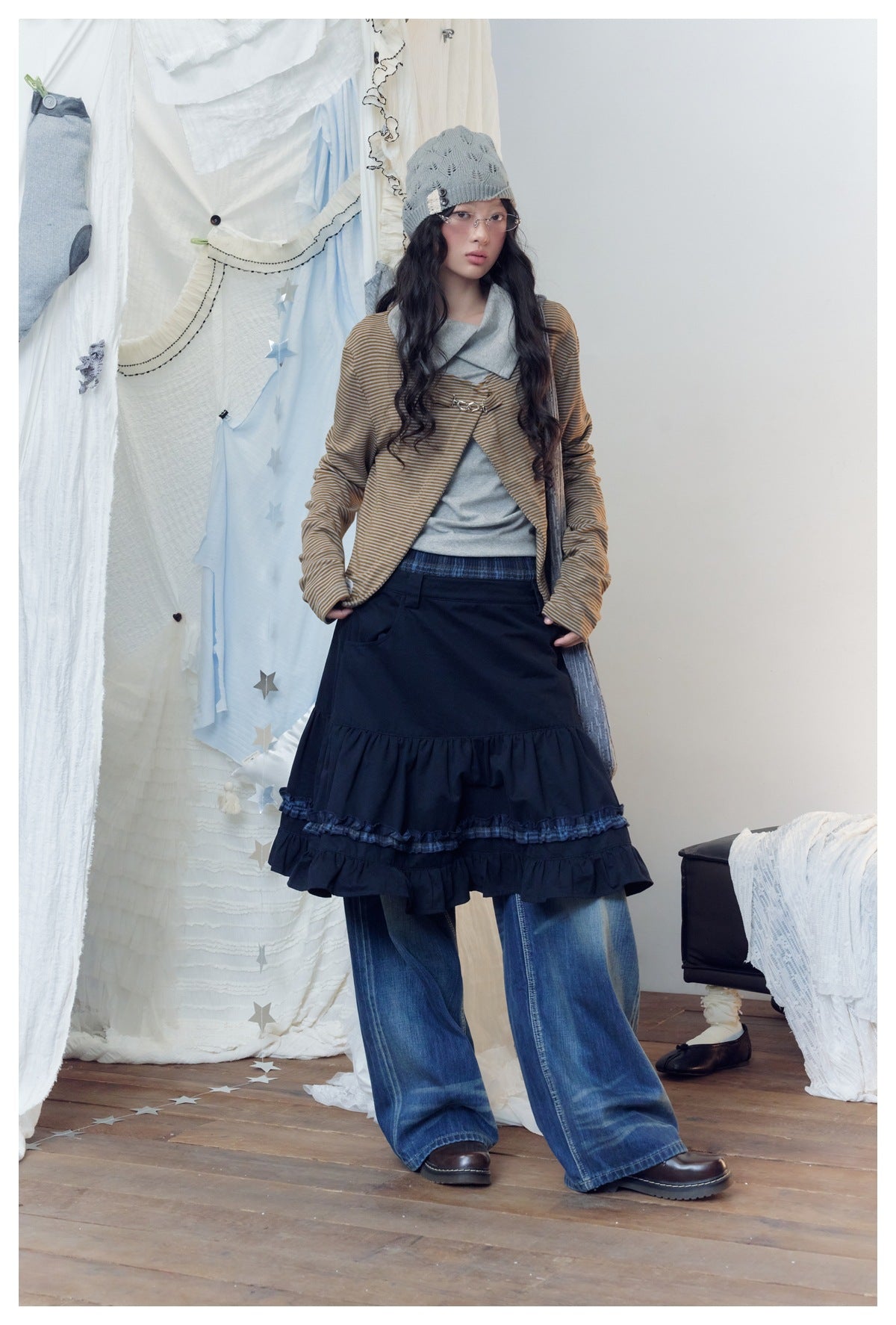 Full-length model wearing a striped jacket, gray top, navy tiered ruffle skirt over wide-leg jeans, and gray knit beanie.