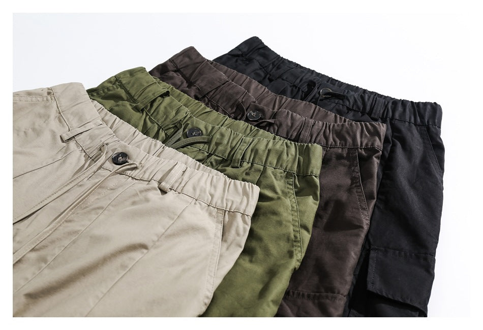 Four pairs of cargo pants in beige, olive green, dark brown, and black, arranged to show elastic waistbands and pockets.