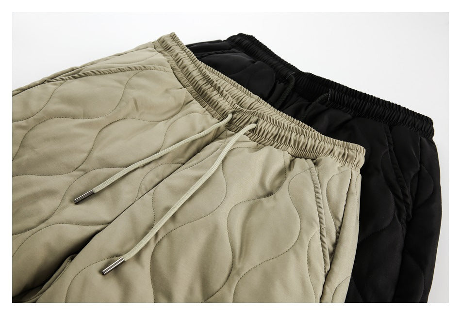 Close-up of olive and black quilted pants with elastic waistbands and drawstrings.