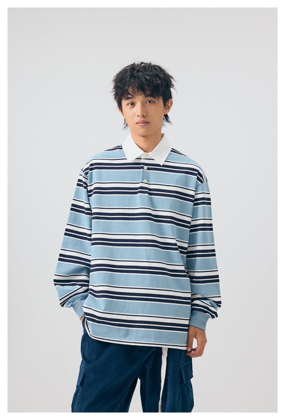 Model wearing a light blue, navy and white striped long-sleeve rugby shirt with a white collar and navy trousers.