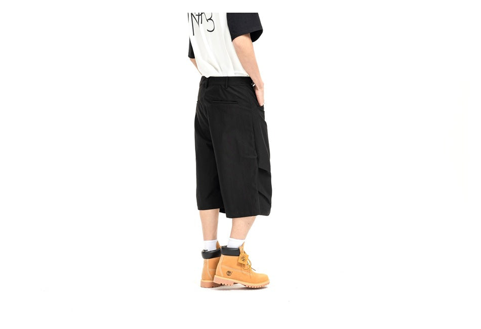 Rear angled view of a model wearing black knee-length shorts, showing a back welt pocket and side cargo pocket.
