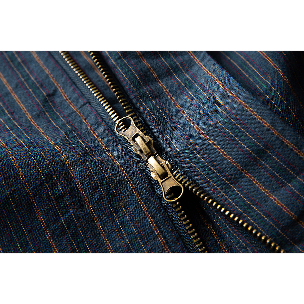 Close-up of a brass-colored two-way zipper on dark blue fabric with multicolored pinstripes.