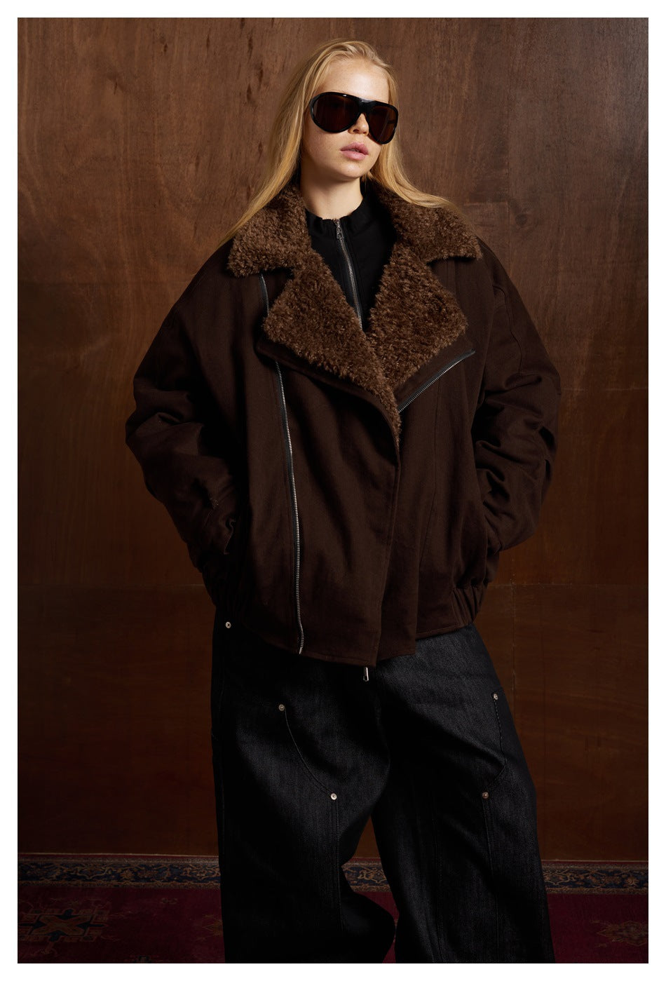 Model wears a dark brown oversized jacket with a wide plush collar and prominent diagonal zipper.