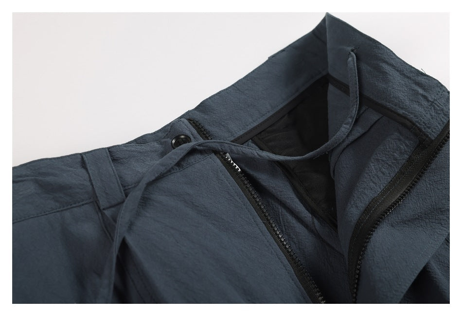 Close-up of blue-gray trousers with the waistband and fly open, showing the zipper and inner drawstring.