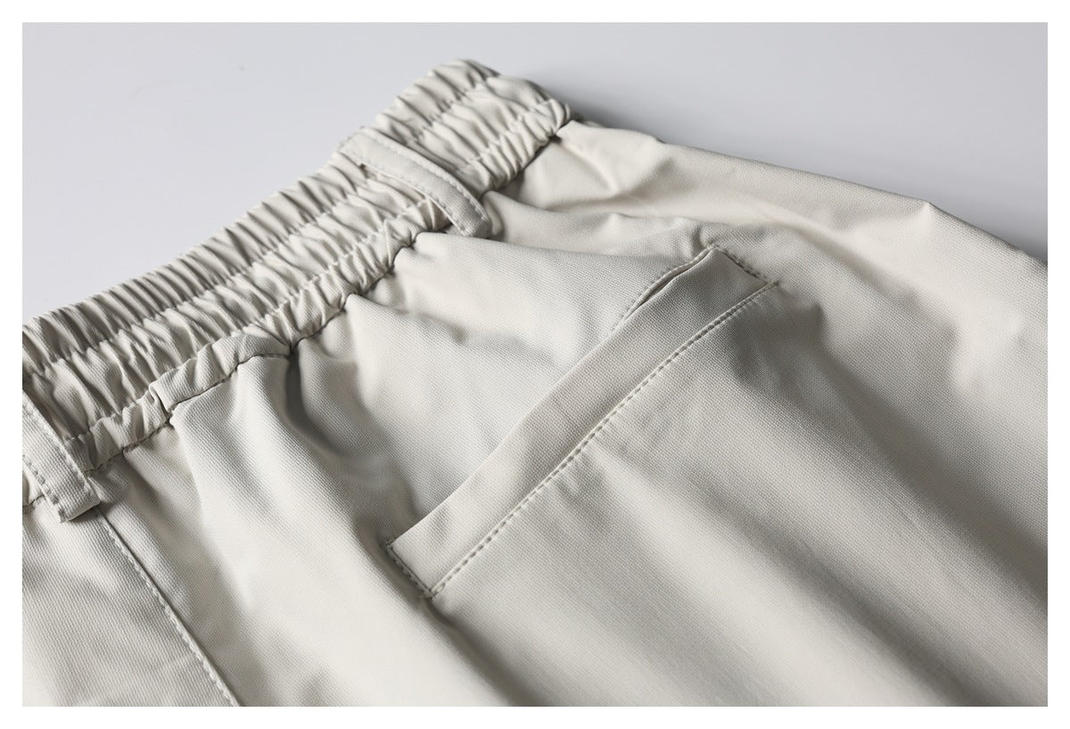 Close-up of light beige pants showing a slanted front pocket and gathered elastic waistband with belt loops.