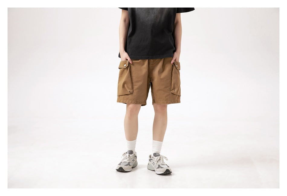Front view of a model wearing brown cargo shorts with large flap pockets, a black T-shirt, white socks and sneakers.