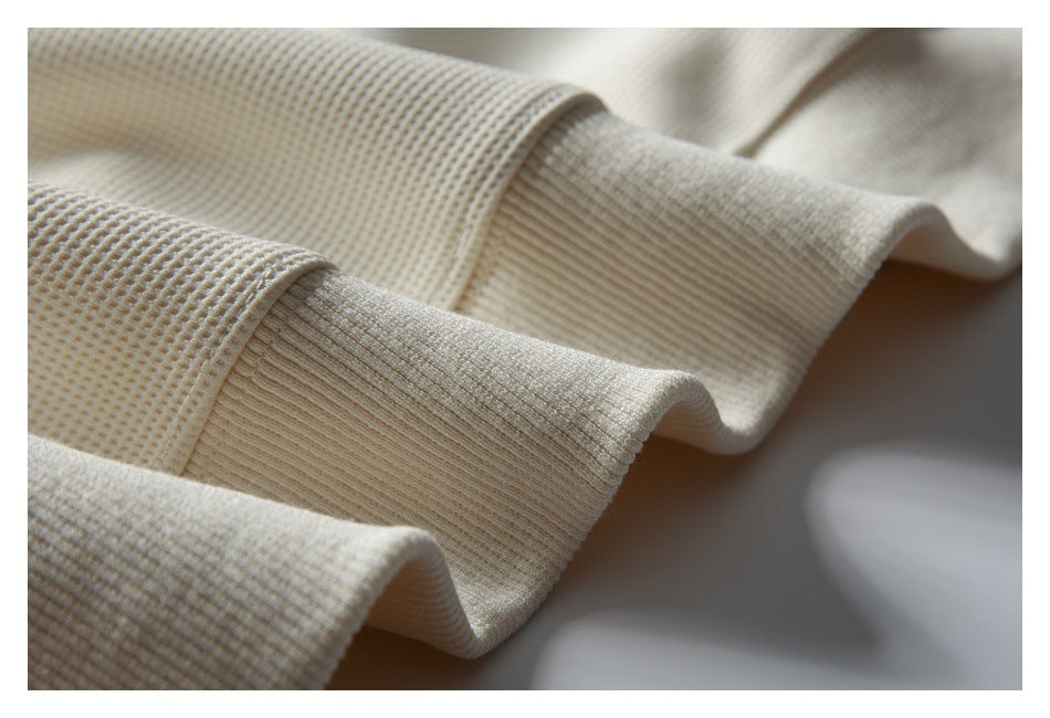 Close-up of cream waffle-knit fabric meeting a wide ribbed edge, showing the texture and seam.