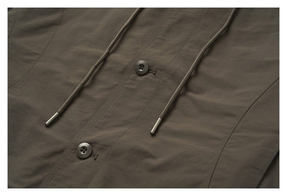 Close-up of the dark olive-brown front with two buttons, long drawcords, and curved seam details.