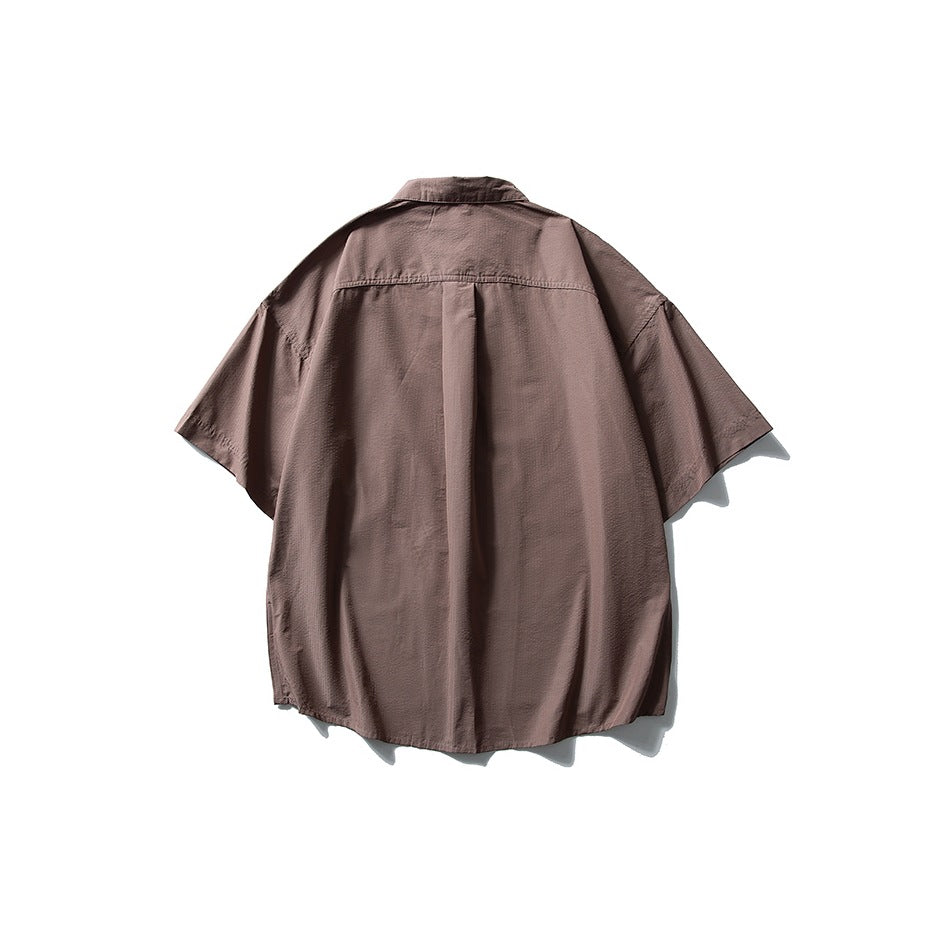 Back view of a dark taupe oversized short-sleeve button-up shirt with a center pleat.