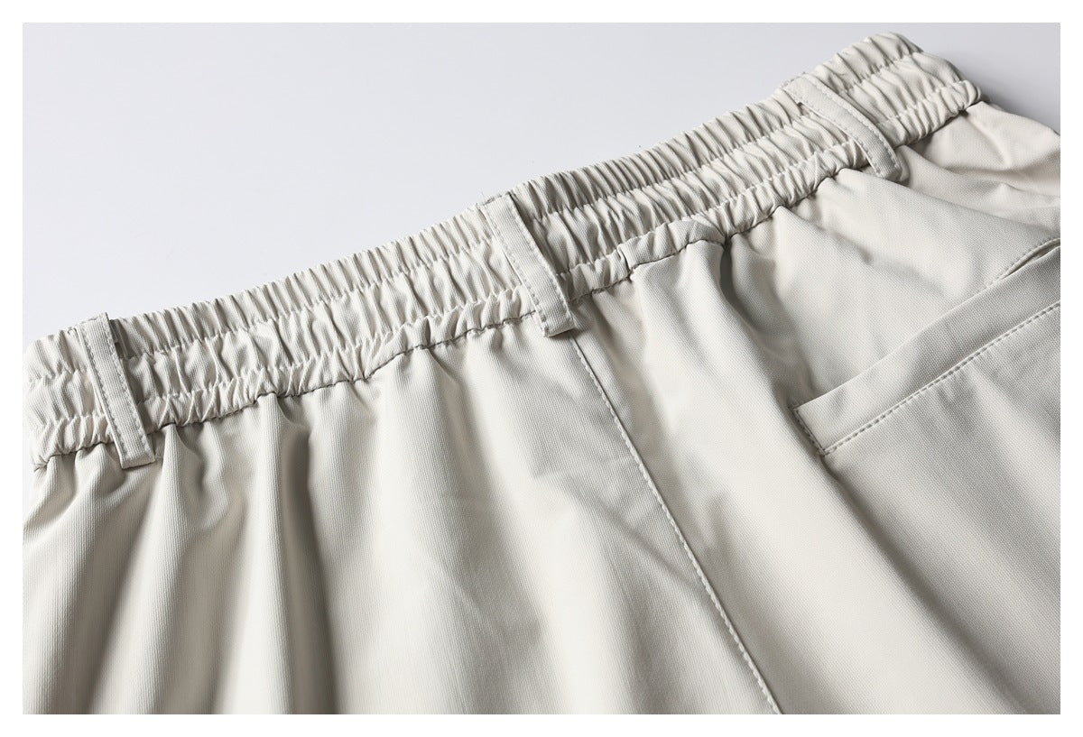 Close-up of light beige pants showing the gathered elastic waistband, belt loops, and side pocket opening.
