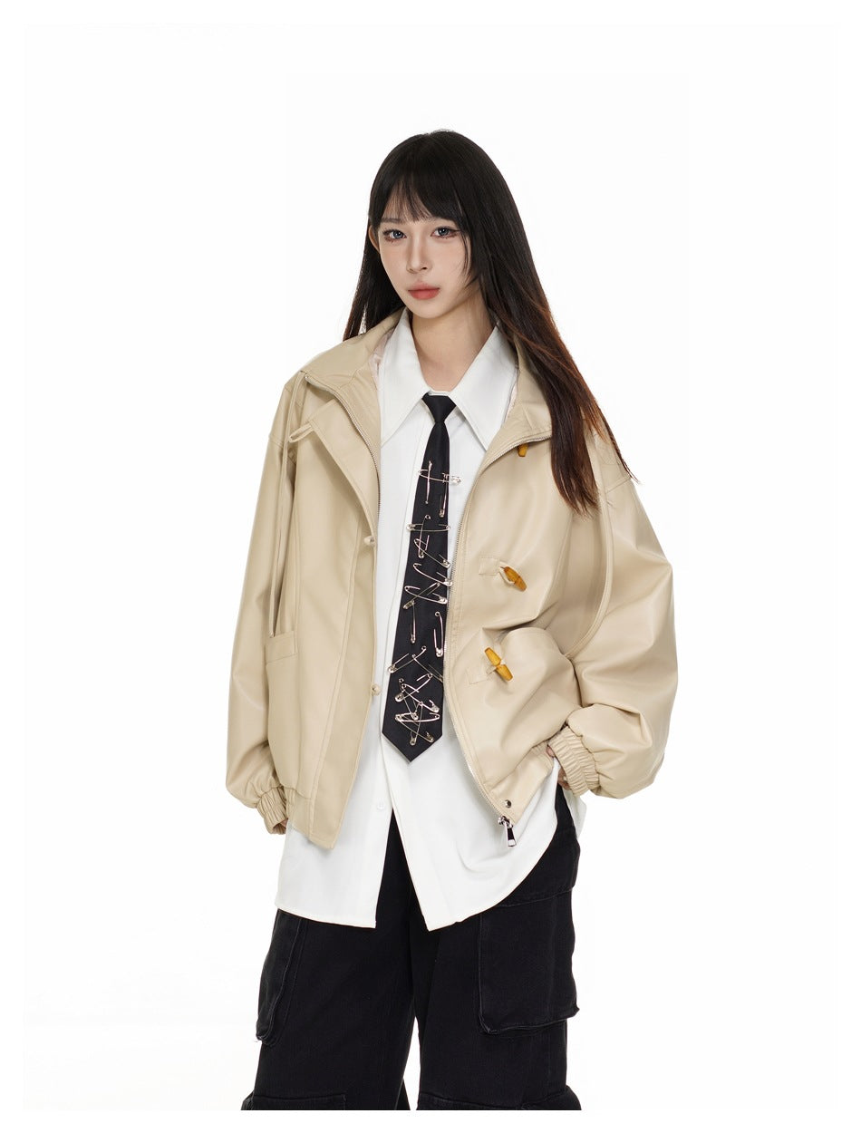 Model wearing an open beige oversized jacket with toggle closures, white shirt, and black tie decorated with safety pins.