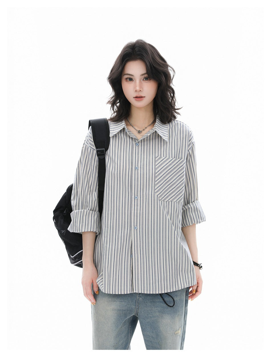 Person wearing a blue striped button-up shirt with sleeves rolled, black backpack strap and light jeans