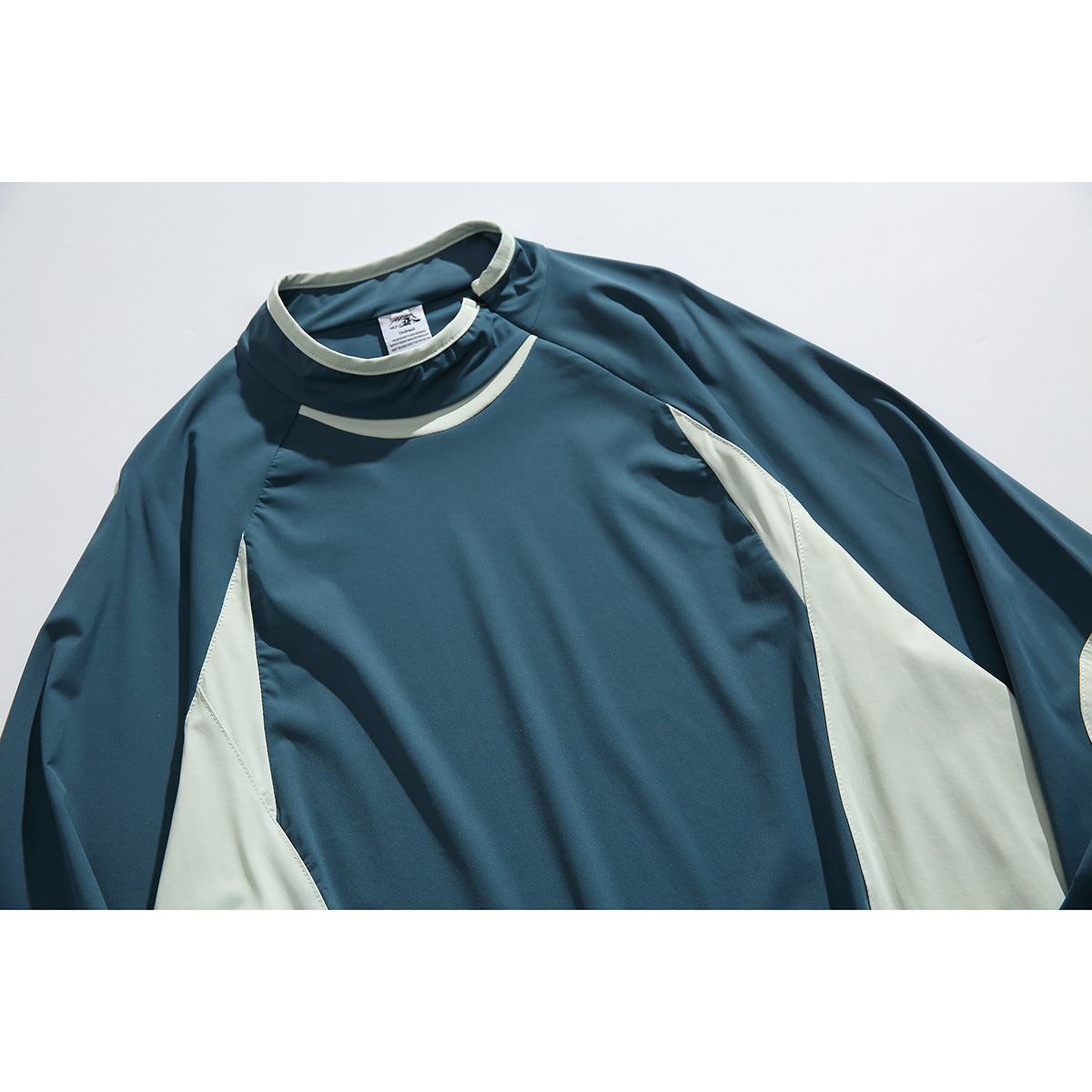 Close-up of a teal pullover with a high collar, pale trim, and contrasting side panels.