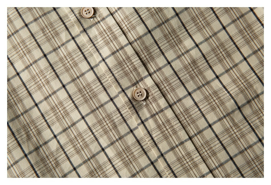 Detail of two beige buttons and the placket on a beige shirt with dark plaid lines.