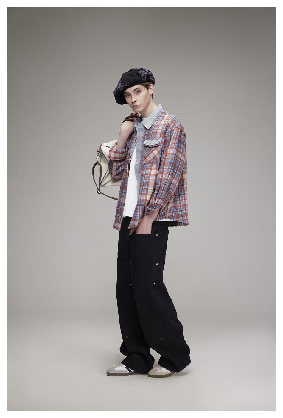Model in a rust, blue and cream plaid button-up shirt, shown at an angle with black trousers and a patterned beret.