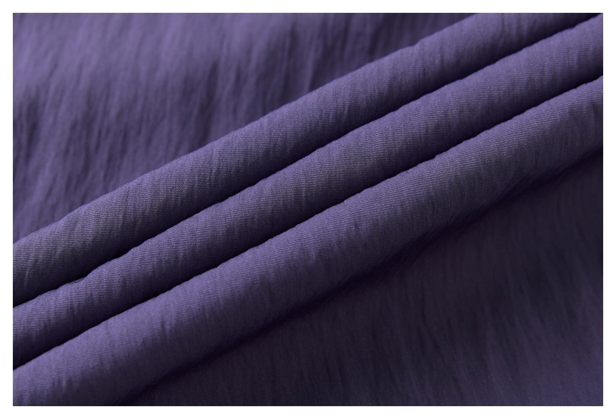 Close-up of dark purple fabric folded into soft ridges, showing a fine woven texture.
