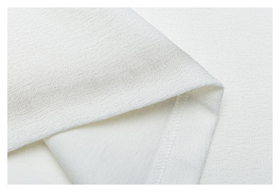 Close-up of a folded white garment hem with visible stitching and textured fabric.