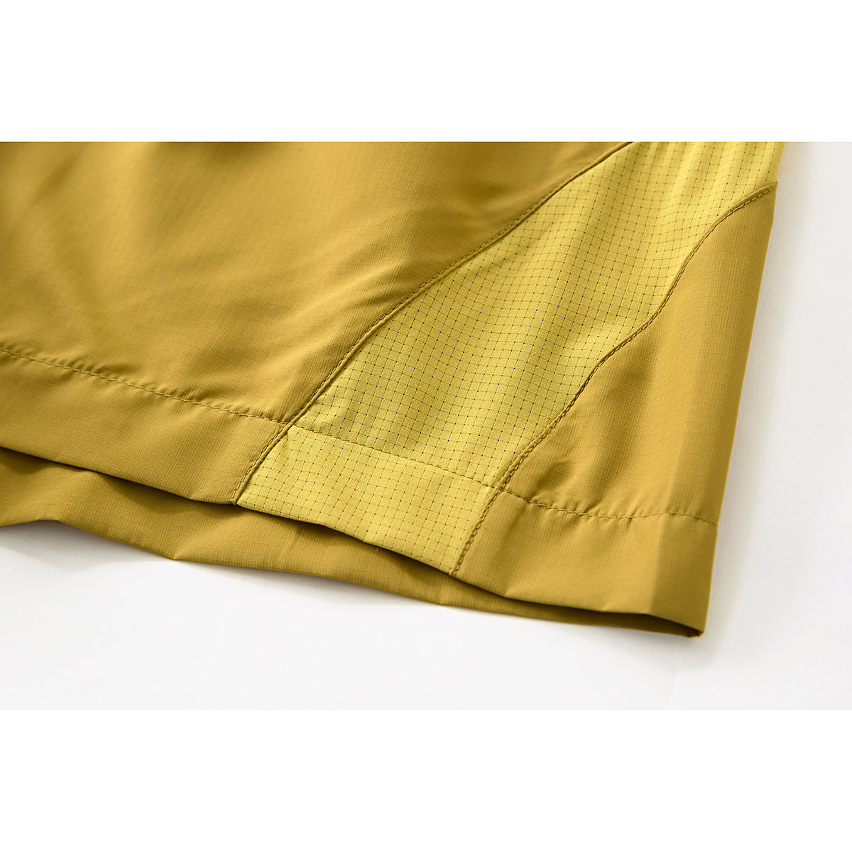 Close-up of mustard-yellow shorts showing a dotted side panel, seams and hem.