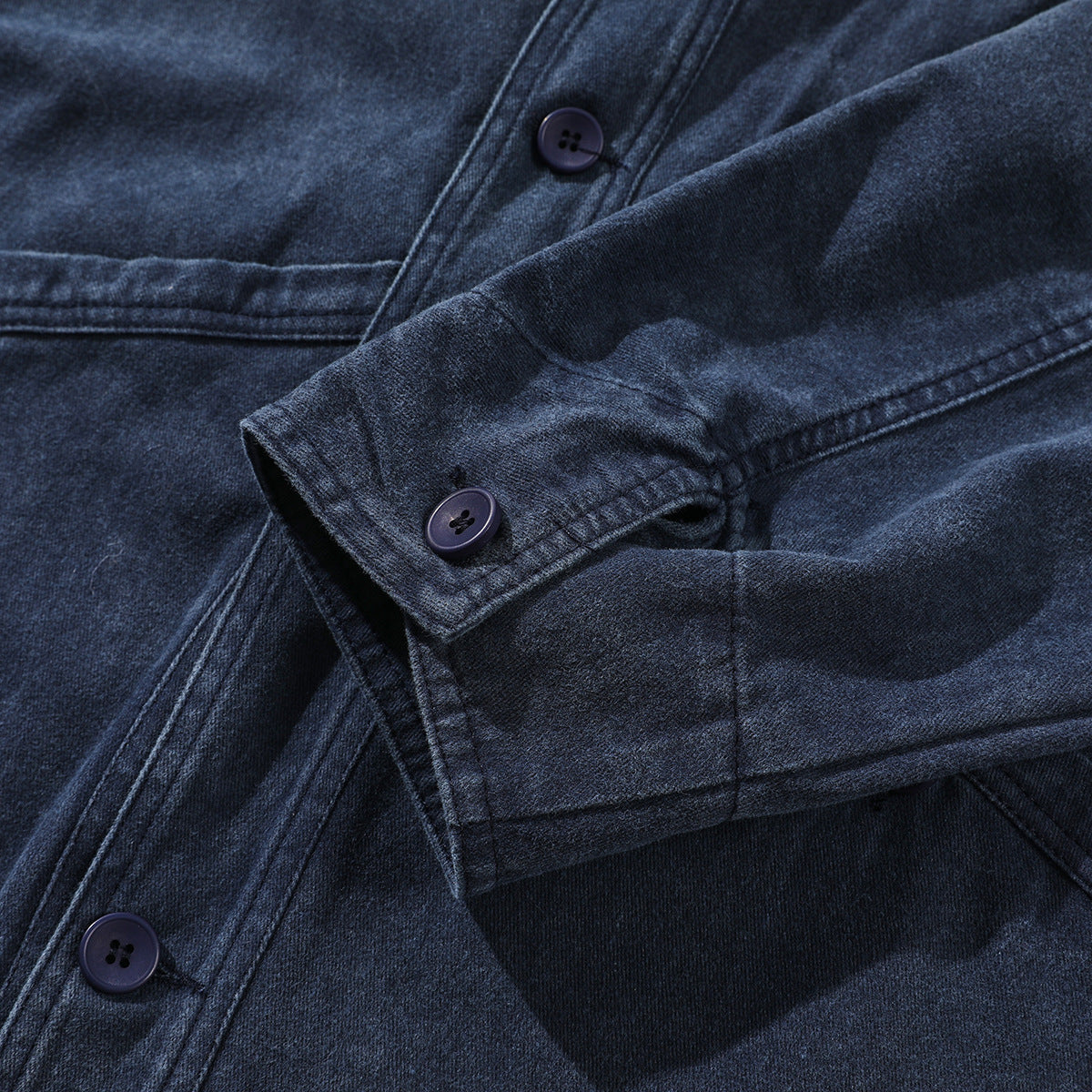 Close-up of a dark indigo jacket with overlapping sleeves, stitched seams, and several dark buttons.