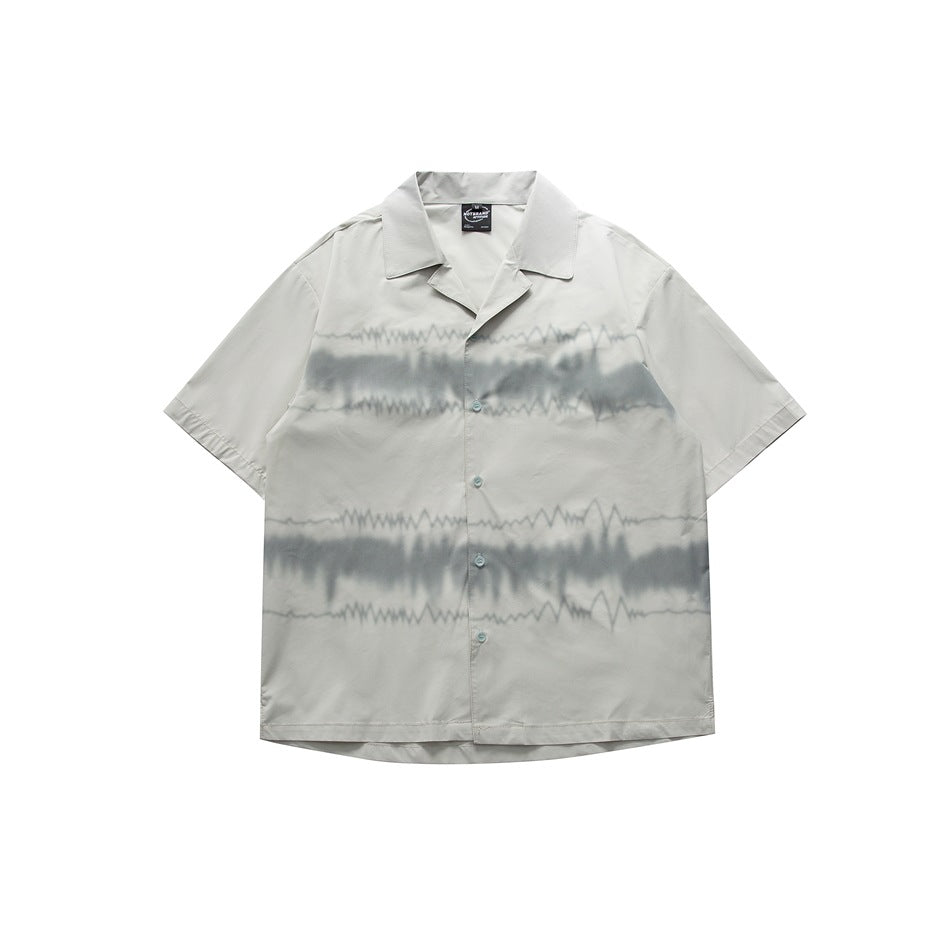 Pale gray-green short-sleeve camp-collar shirt with blurred gray wave print across the front, flat lay