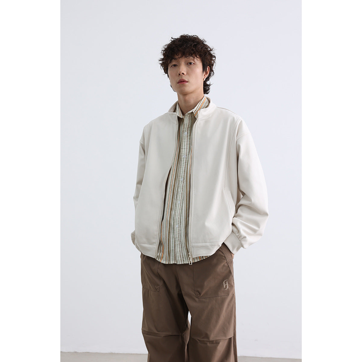 Model wearing an off-white stand-collar zip jacket over a striped shirt, shown from the waist up.
