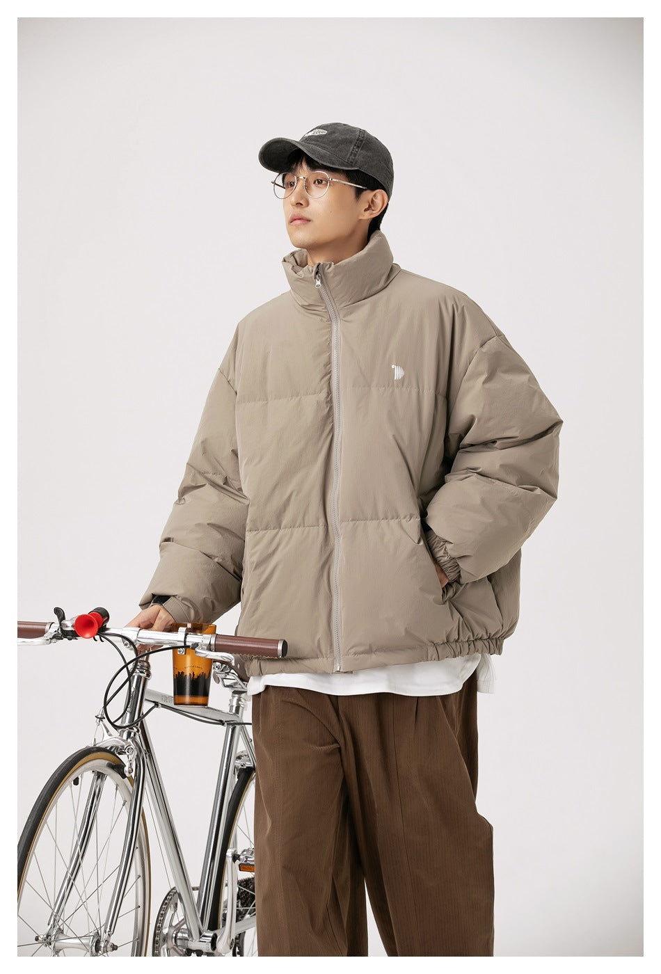 Closer view of a model wearing a taupe high-collar puffer jacket beside a bicycle.