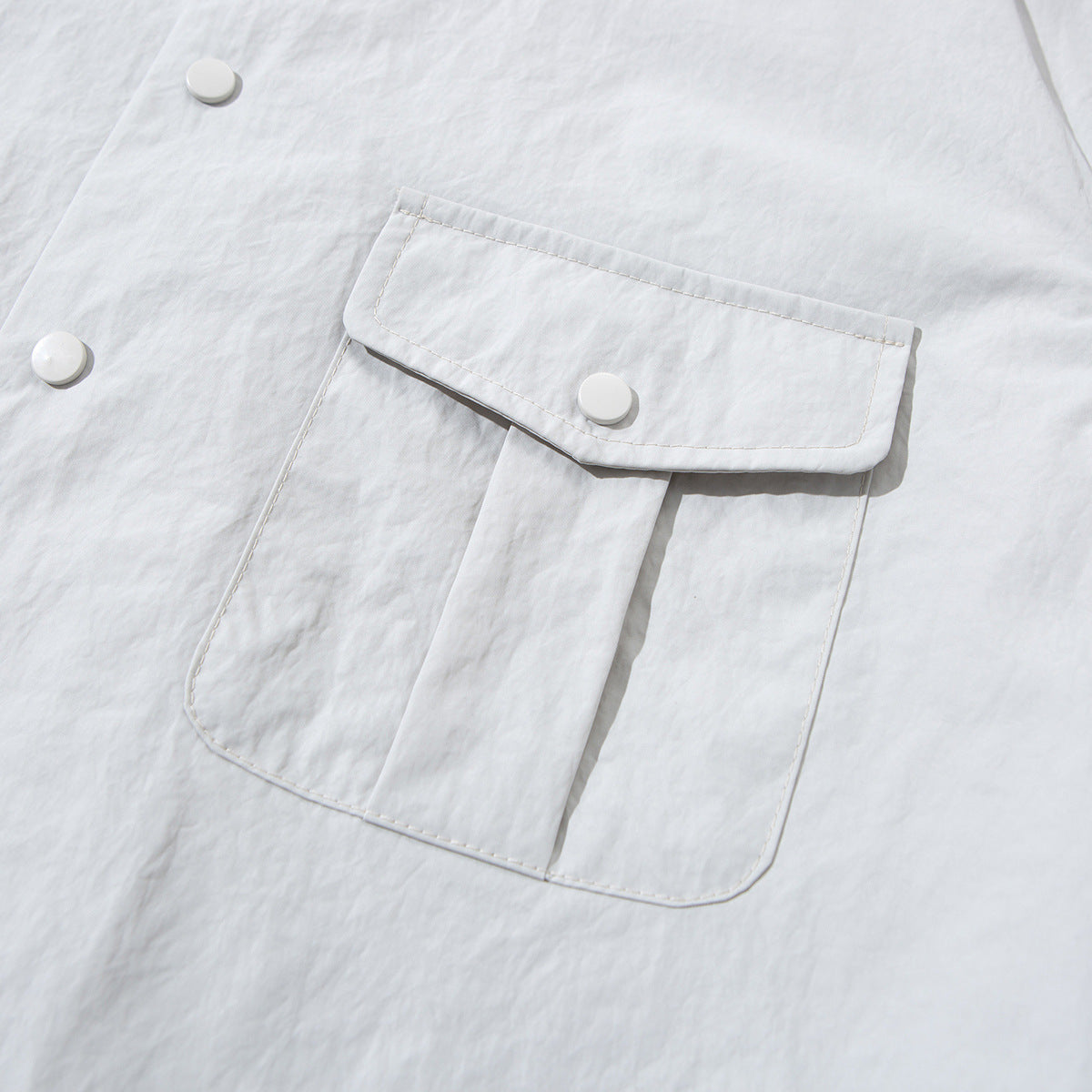 Close-up of a pale gray jacket's large flap pocket with a white snap button and visible stitching.