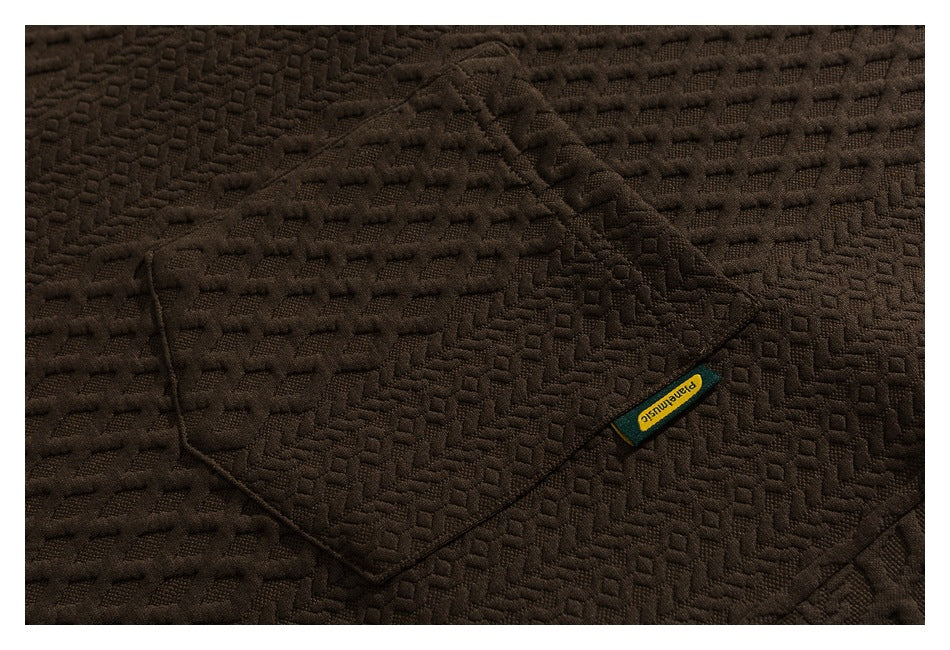 Close-up of a brown jacket's textured fabric, stitched pocket, and small sewn label.