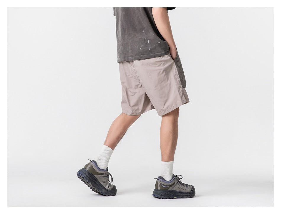 Model wearing light taupe shorts, shown from the side and rear while walking.
