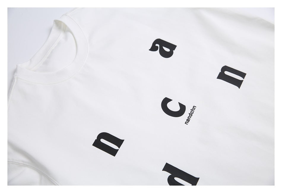 Close-up of a white T-shirt with scattered black letters and small “nandchn” text.