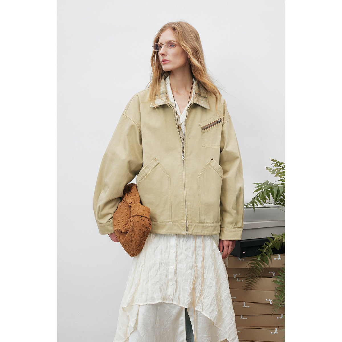 Model wearing a beige zip-front jacket with a plaid collar, shown over a white layered outfit.