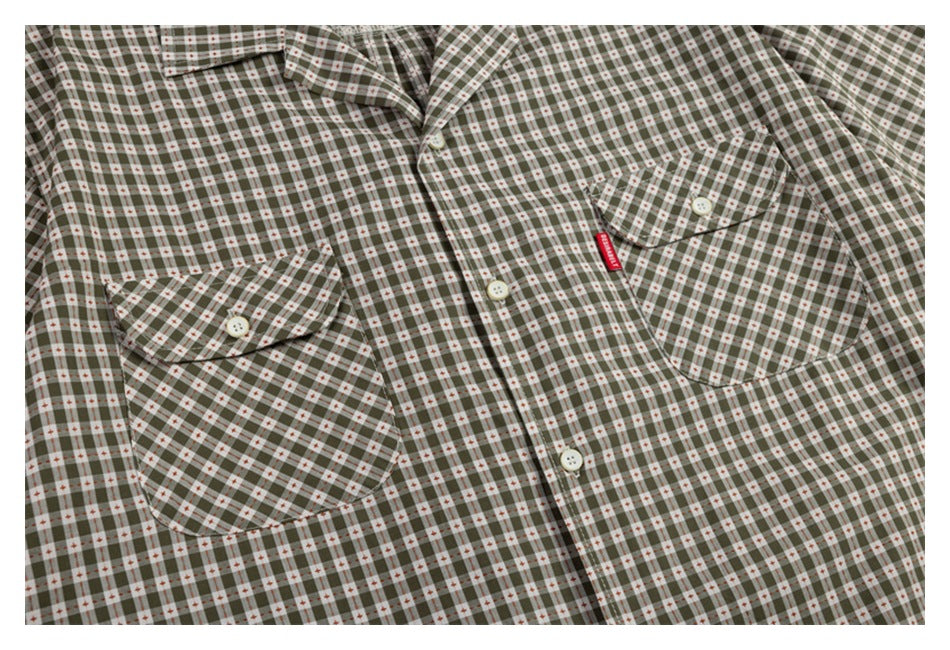 Close-up of a gray-green check shirt front with two buttoned chest pockets and a small red tab.