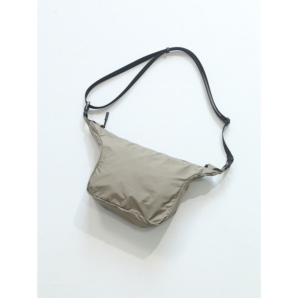Khaki beige crossbody bag with black adjustable strap and plastic buckles on a light background