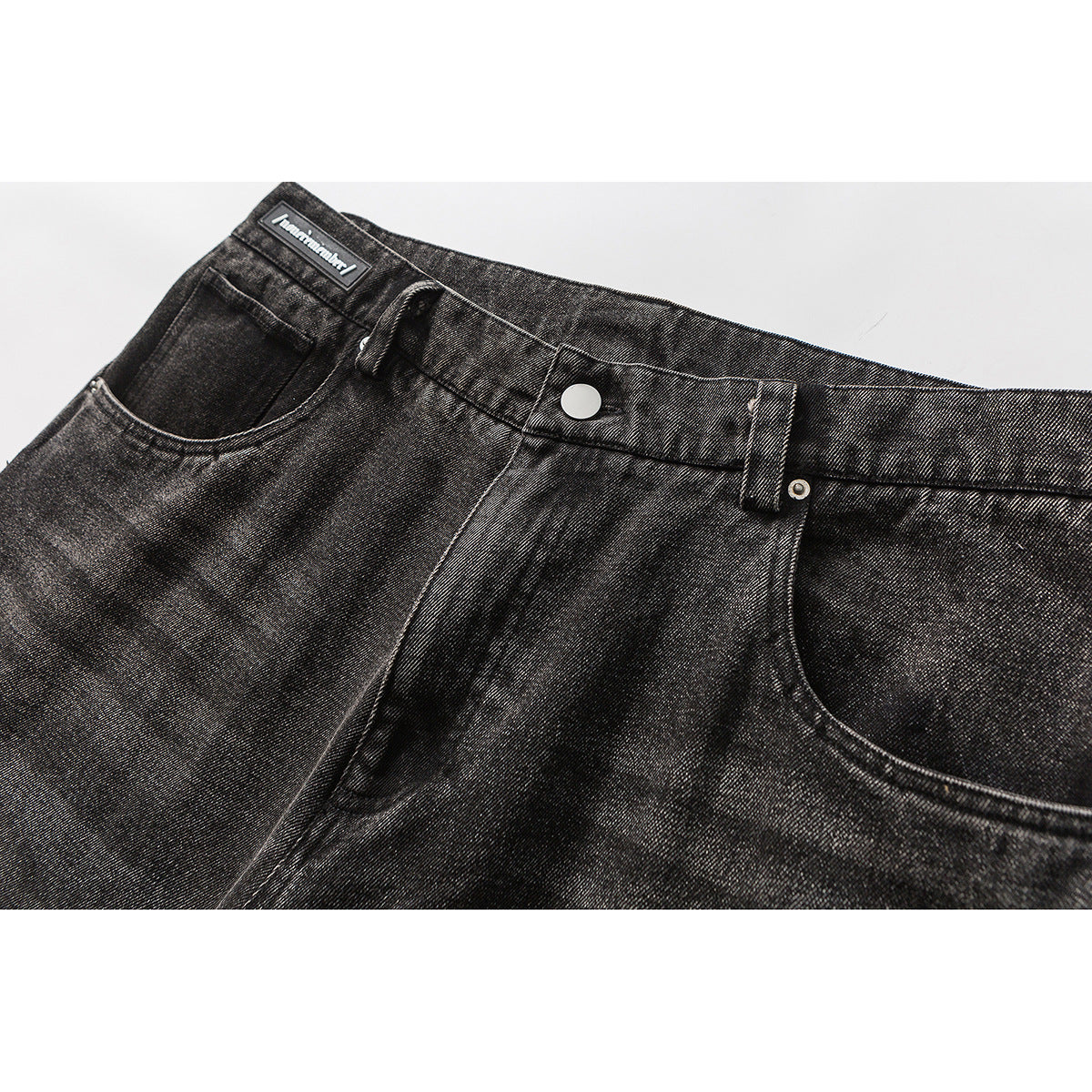 Close-up of the front waistband, button, belt loops and pockets on washed black jeans.