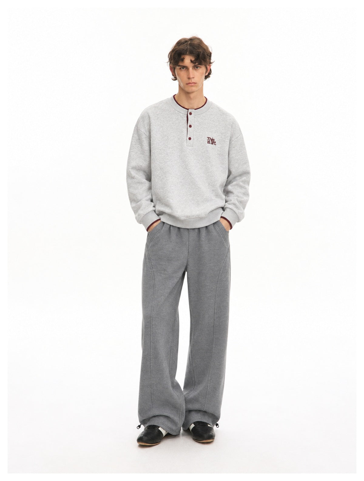 Full-length front view of a model wearing a light gray Henley sweatshirt and wide-leg gray trousers.