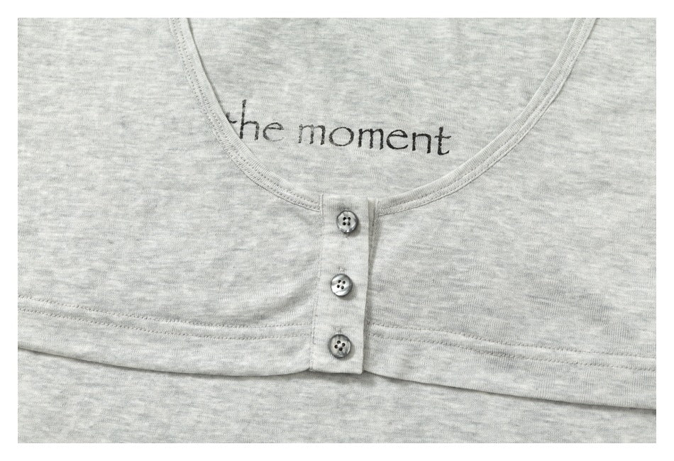 Close-up of a heather-gray garment's rounded neckline, three-button placket, and small 'the moment' print.