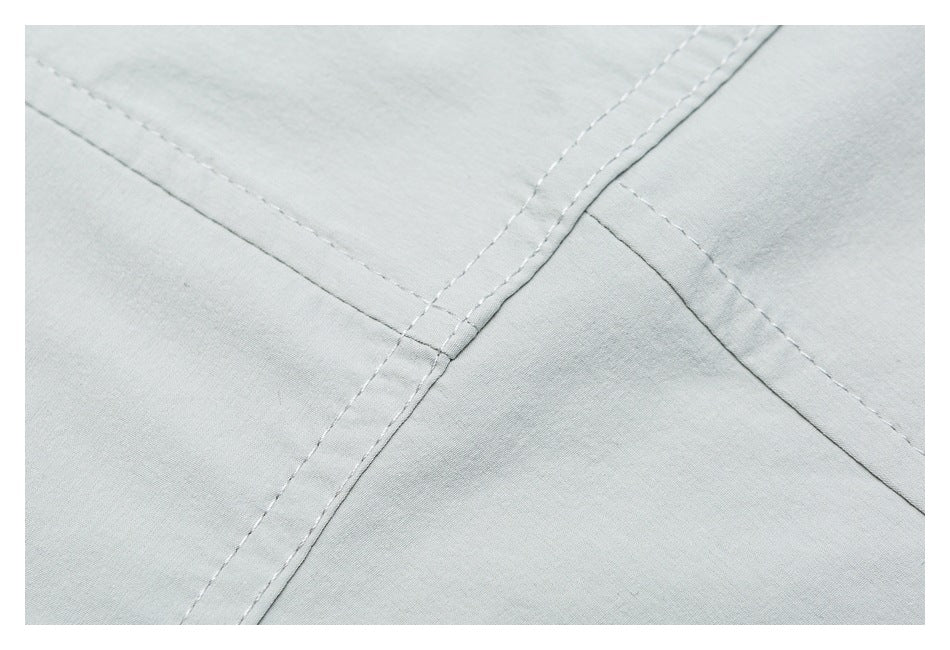 Close-up of intersecting stitched seams on pale gray garment fabric.