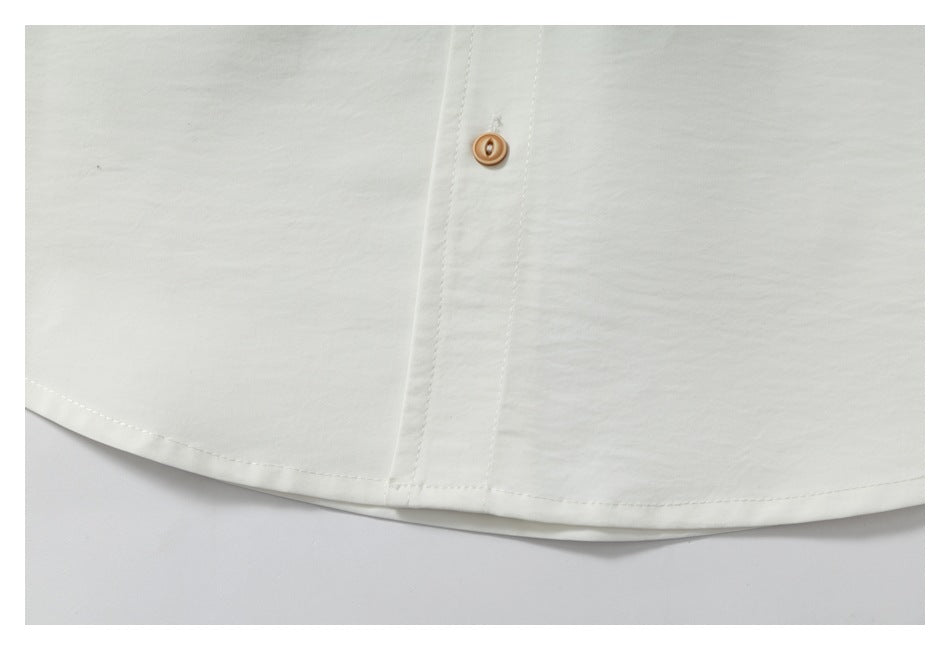 Close-up of the curved hem and tan-button placket of an off-white garment.