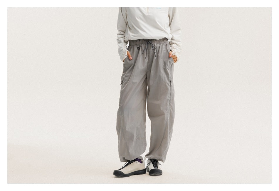 Front view of a model wearing light-gray loose drawstring pants with side pockets and elasticized cuffs.