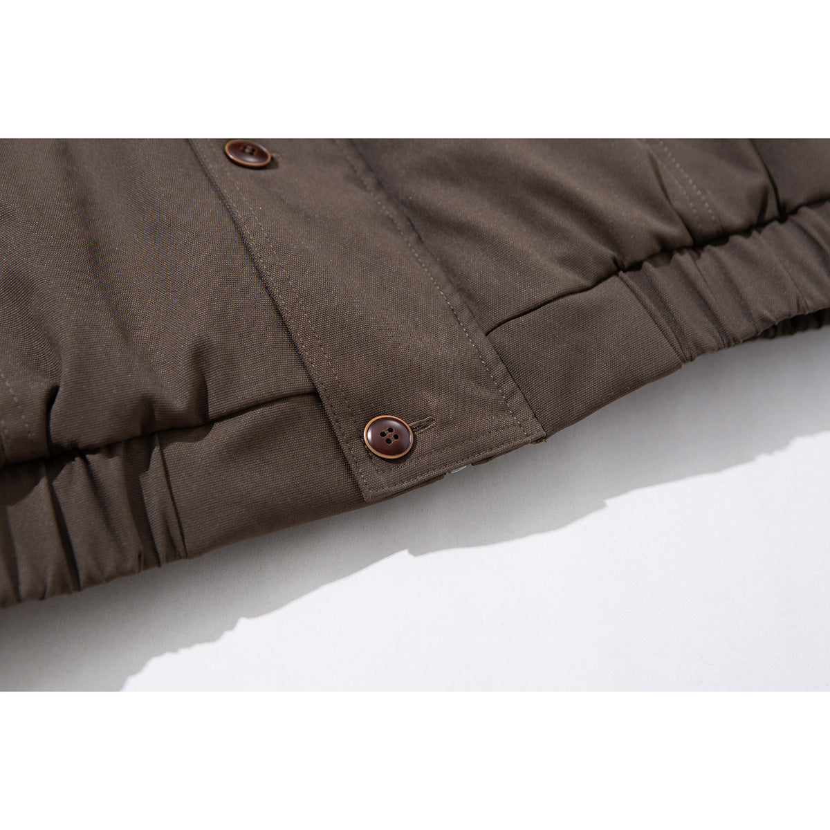 Close-up of the dark brown jacket's gathered hem and buttoned placket tab.