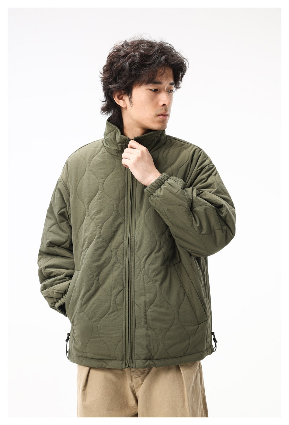 Man wearing an olive quilted jacket and holding the collar near the zipper, shown from the front at close range.