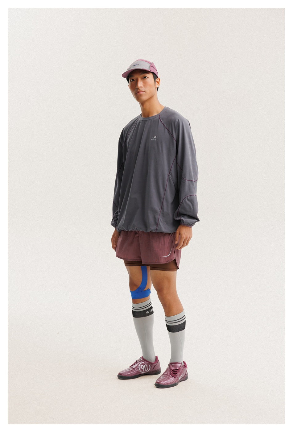 Three-quarter view of a model wearing a charcoal gray pullover with plum seam details and mauve athletic shorts.