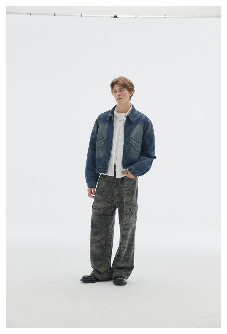 Front view of a model wearing a dark blue denim jacket, white layers, and loose camouflage cargo pants.