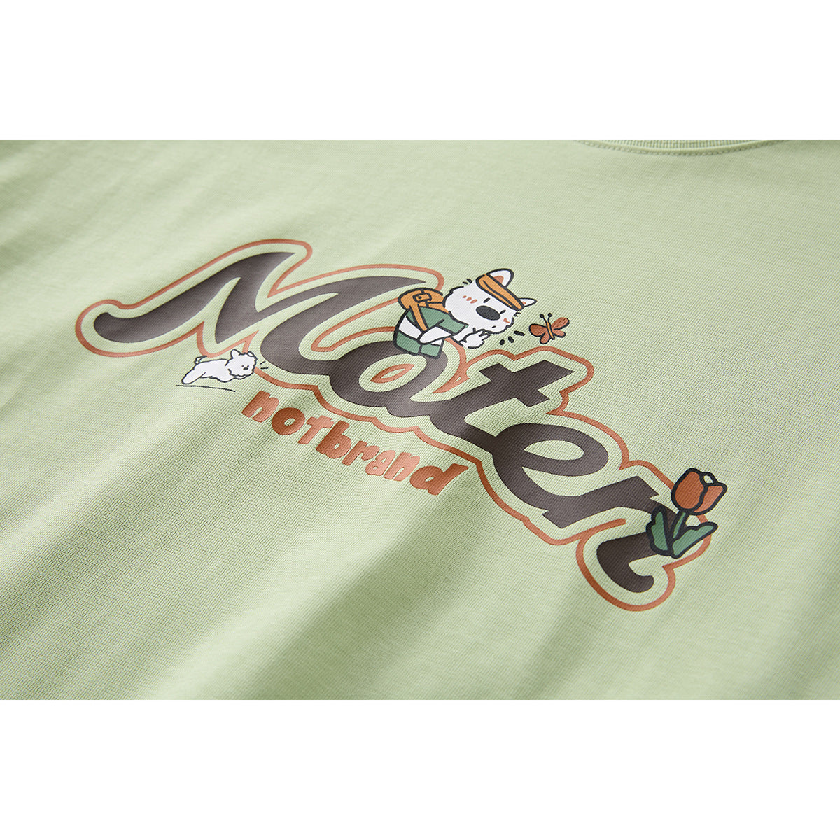 Close-up of a pale green T-shirt graphic with stylized lettering, cartoon cats, and a flower.