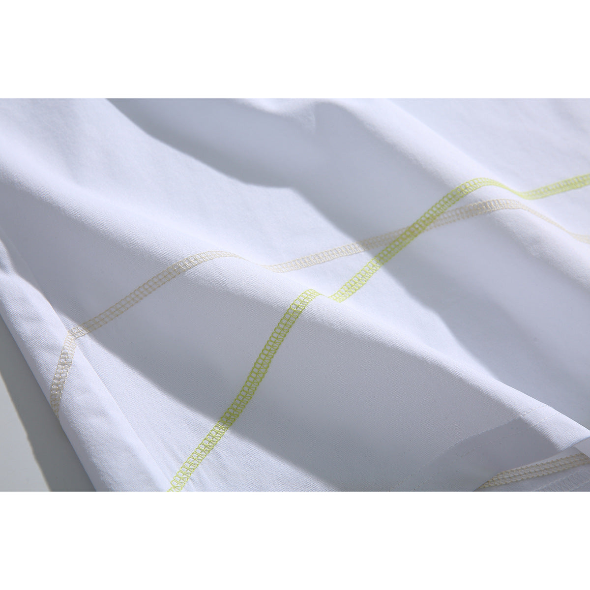 Close-up of curved lime and pale contrast overlock stitching on white fabric.