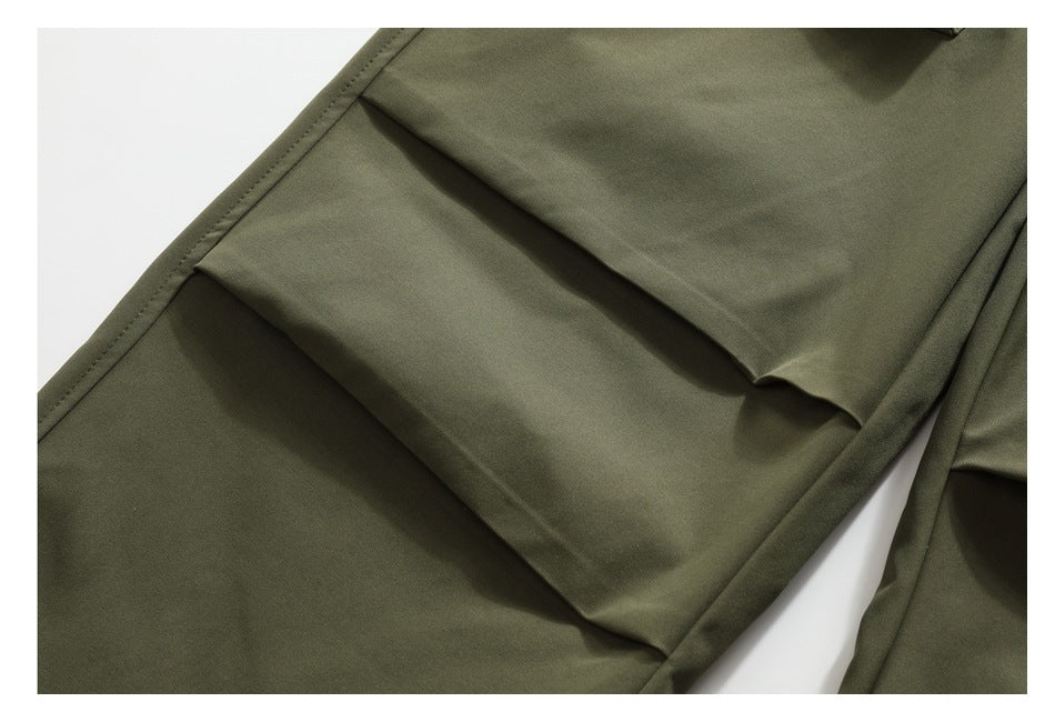 Close-up of layered flap cargo pockets on olive pants, showing the stitching and folded construction.