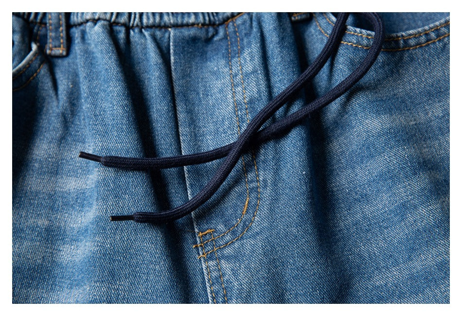 Close-up of blue denim shorts with a gathered waistband, dark drawstrings, and contrasting tan stitching.