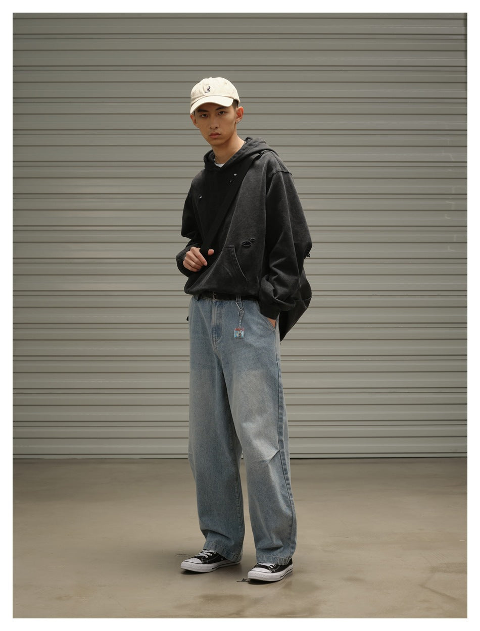 Model wearing a black distressed hoodie, pale blue wide-leg jeans, a cream cap and a black crossbody bag.